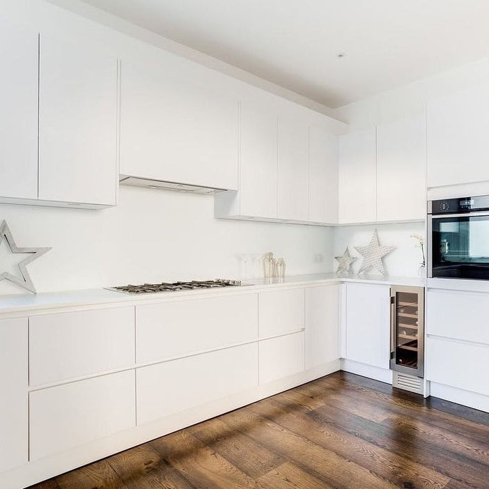 Sleek minimalist white kitchen design featuring a 74cm integrated extractor fan, gas stovetop, and dark wood flooring