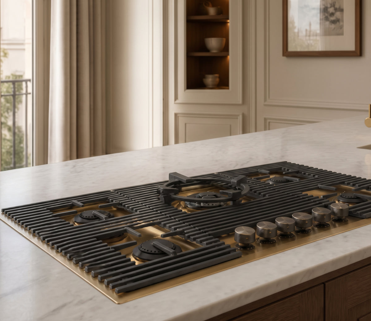 A built-in gas cooktop with black grates and control knobs over a brushed brass base, installed into a white marble kitchen island countertop. flush to worktop