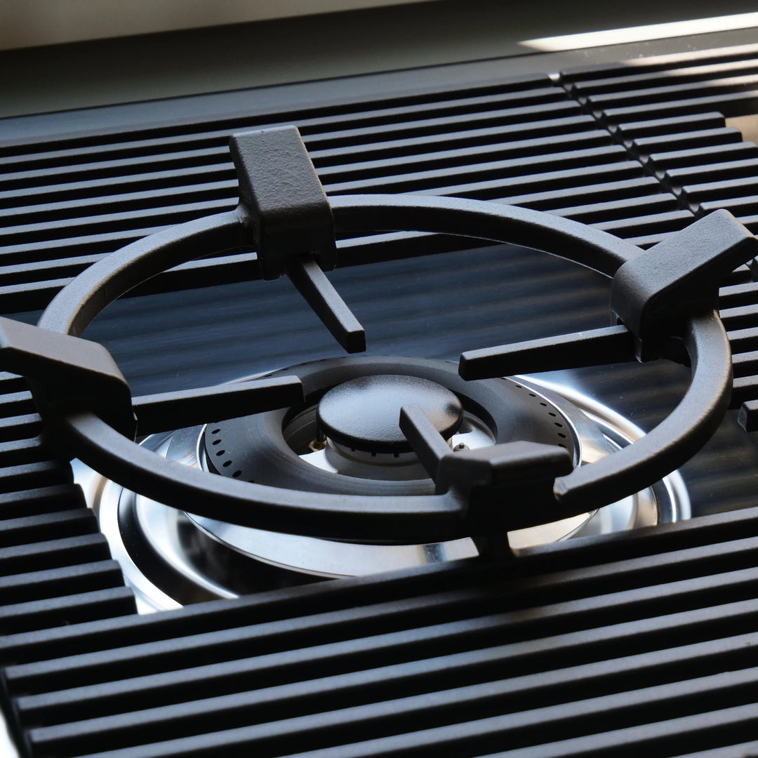 Close-up of a black cast iron gas burner grate over a stainless steel gas stove burner.
