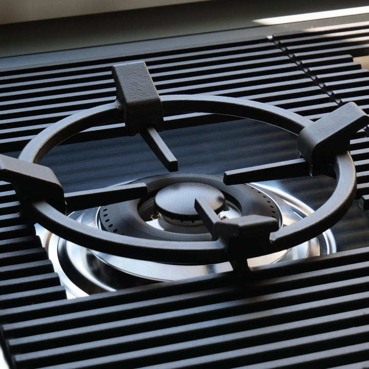 Close-up of a black cast iron gas burner grate over a stainless steel gas stove burner.