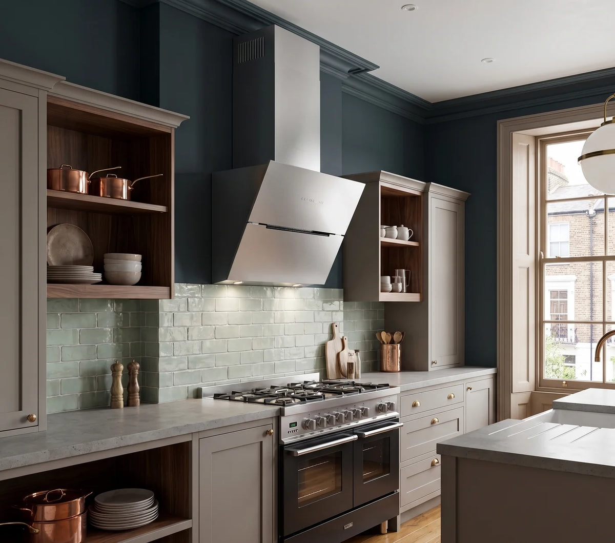Stainless steel Ascenti angled wall cooker hood in a modern kitchen with dark cabinets, stainless steel appliances, and a large window.