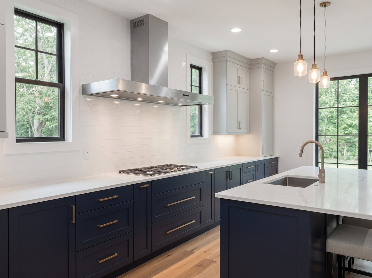 A modern kitchen interior with navy blue cabinets, white countertops, a stainless steel range hood, wood flooring, and pendant lights over a sink island.