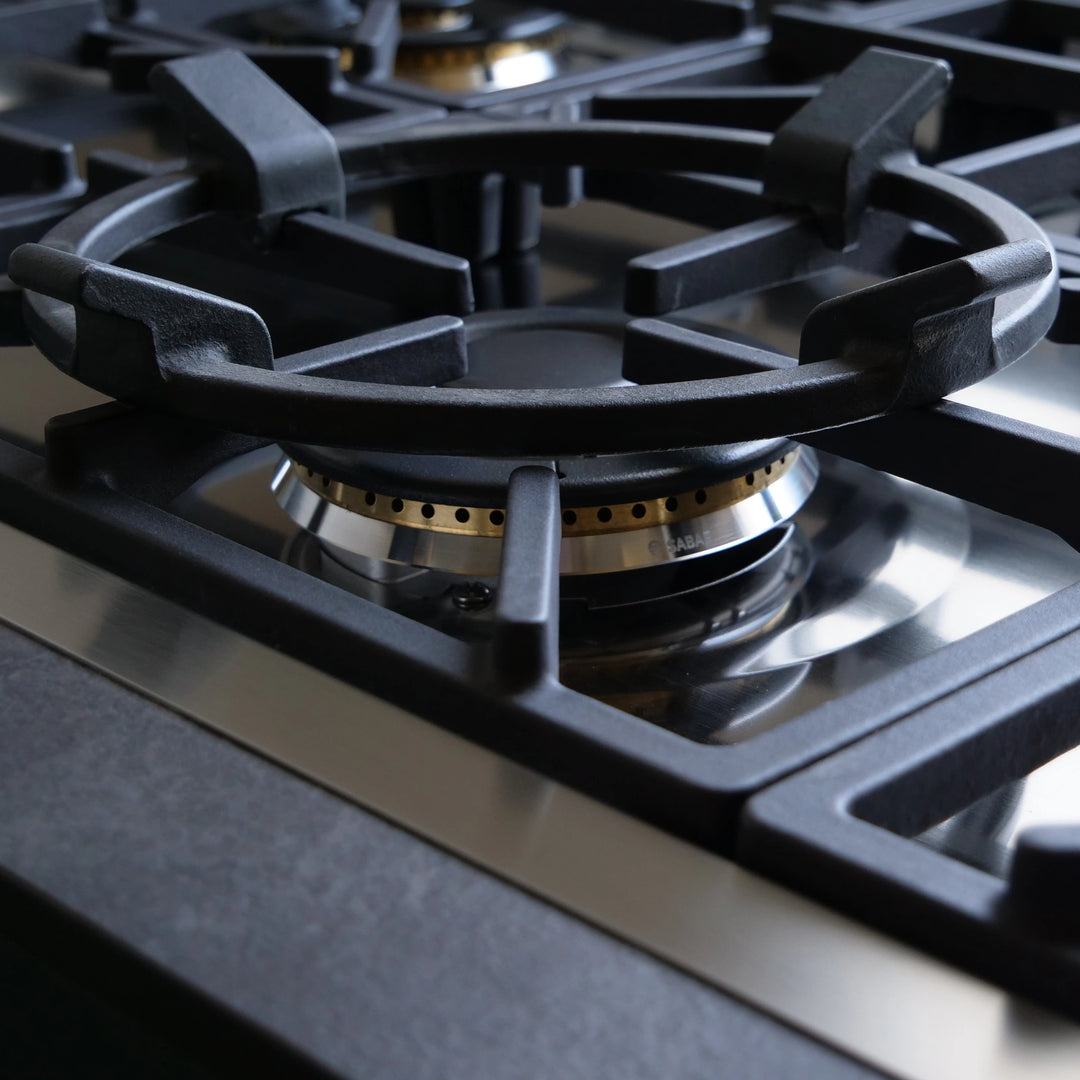 Close-up of a black cast-iron gas stovetop burner grate over a stainless steel and gas flame burner on a modern gas range.