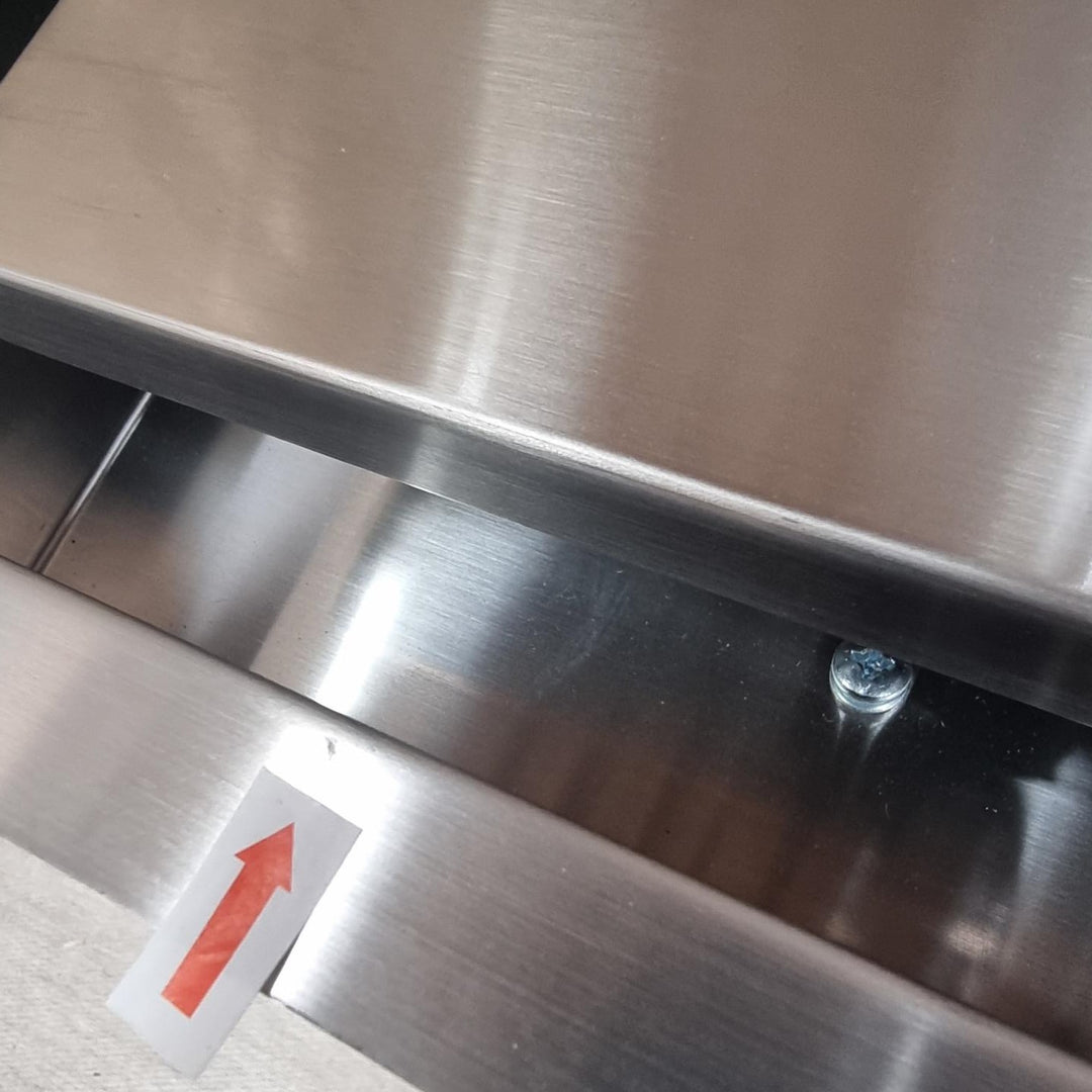 Close-up of brushed stainless steel metal surfaces with a small red arrow sticker on the lower left and a visible screw fastener.