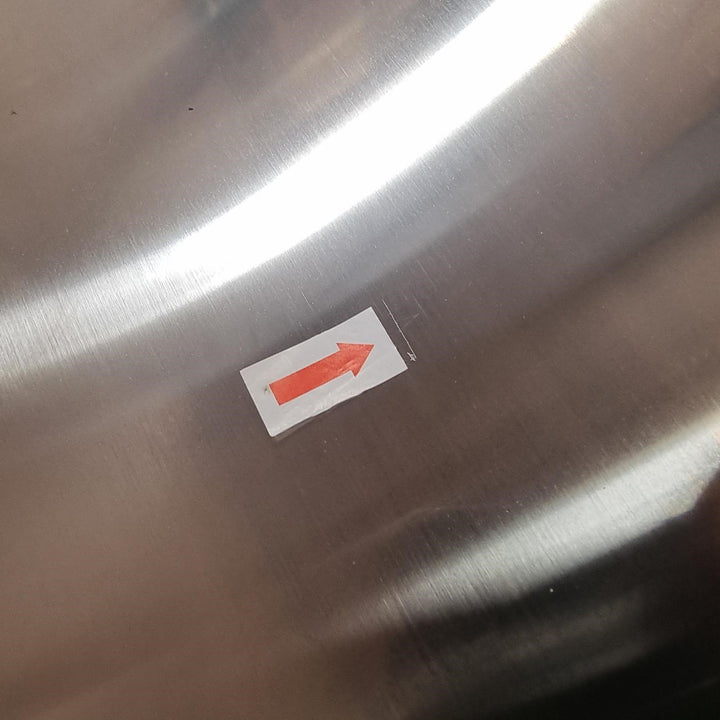 A small white rectangular sticker with a red arrow pointing to the right, placed on a brushed stainless steel surface.