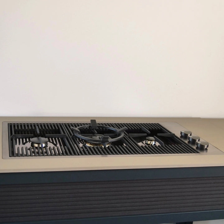 An 87cm Milano Lusso 3 Burner Stainless Steel Gas Hob on with a beige countertop, black cast iron grates, and silver control knobs